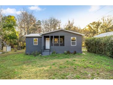 Cozy gray house with a covered front porch and white trim, surrounded by a green lawn and mature trees at 21055 Highway 441 N, Micanopy, FL 32667