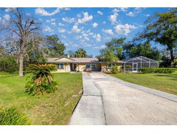 Inviting single-story home with a long driveway and a screened-in patio, surrounded by mature trees and lush landscaping at 3301 Se 32Nd Ave, Ocala, FL 34471