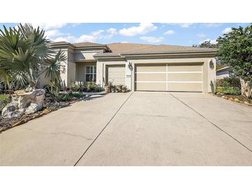 Beige two-car garage home with a well maintained lawn, landscaping, and concrete driveway at 13424 Se 89Th Terrace Rd, Summerfield, FL 34491