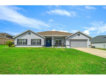 Charming one-story home with lush green lawn and a blue front door with a gray exterior and two car garage at 6875 Se 11Th Pl, Ocala, FL 34472