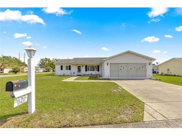 Well-maintained single-story home with a green lawn and a two-car garage featuring a large driveway on a beautiful sunny day at 17421 Se 107Th Ct, Summerfield, FL 34491