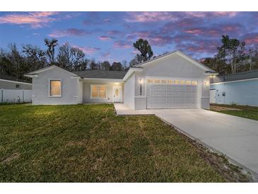 Charming single-story home boasts a manicured lawn, attached garage, and modern architectural design at dusk at 12882 Se 42Nd Ct, Belleview, FL 34420