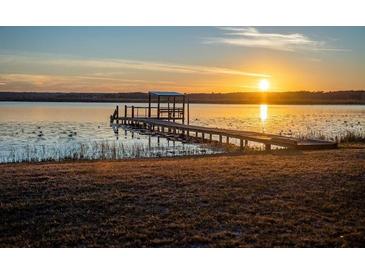 Waterfront view featuring a dock with seating during a colorful sunset overlooking a serene lake at 14540 Ne 250Th Ave, Fort Mc Coy, FL 32134