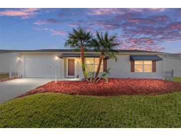 Charming home exterior with manicured lawn, colorful mulch, and young palm trees at dusk at 2013 Cardona Way, The Villages, FL 32159