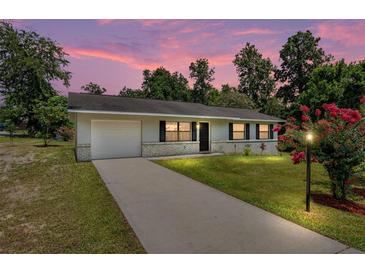 Charming one-story home with brick accents, green lawn, and lovely landscaping at sunset at 23 Juniper Pass Ln, Ocala, FL 34480