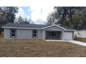 Charming single-story home with gray stucco, a modern roof, an attached garage, and a well-manicured lawn at 734 Nw 57Th Ave, Ocala, FL 34482