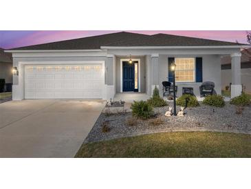 Charming single-story home featuring a well-manicured lawn, an attached garage, and a welcoming front porch with rocking chairs at 7698 Sw 85Th Cir, Ocala, FL 34481