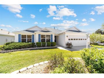 Charming single-story home with white siding, blue shutters, well-manicured lawn, and a two-car garage at 1854 Oxford Lane, The Villages, FL 32162
