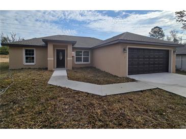 Tan, one-story home with a dark garage door and walkway leading to the front door at 13 Locust Trak, Ocala, FL 34472