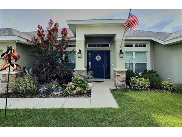 Inviting home entrance featuring a blue front door, decorative plants, and an American flag waving above at 1034 Se 65Th Cir, Ocala, FL 34472