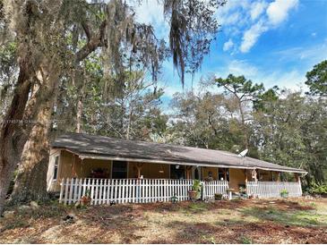 Ranch-style home featuring a charming white picket fence and a covered porch, shaded by mature trees and Spanish moss at 1370 Nw 120Th Ave, Ocala, FL 34482