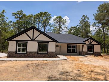 Charming single-story home featuring black trim, stone accents, and a well-maintained lawn surrounded by mature trees at 6150 Sw 123 Ave Rd, Dunnellon, FL 34432