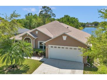 An exterior view of a tan home featuring a two-car garage, manicured lawn, and scenic lake backdrop at 1201 Creekview Ct, St Cloud, FL 34772