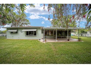 Charming single-story home with a covered patio, lush lawn, and mature trees, offering serene outdoor living at 12180 Maple St, Dunnellon, FL 34432