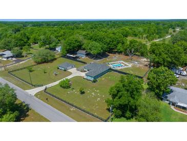 Aerial view of a home with a pool, large yard, a detached garage and surrounded by lush trees at 2563 Se 156Th Place Rd, Summerfield, FL 34491