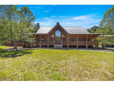 Stunning log cabin home with a metal roof and a large front porch, set against a backdrop of lush greenery at 3360 Se 183Rd Avenue Rd, Ocklawaha, FL 32179