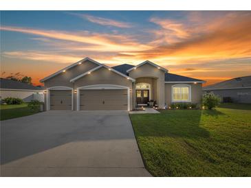 Inviting home exterior featuring a well-manicured lawn and a two-car garage against a breathtaking sunset sky at 9074 Se 48Th Court Rd, Ocala, FL 34480