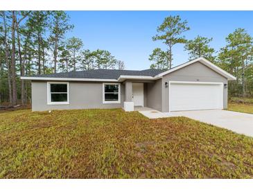 Charming single-story home featuring a gray exterior, attached garage and naturally landscaped front yard surrounded by trees at 24354 Nw Water Oak Ave, Dunnellon, FL 34431