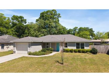 Charming single-story home with a well-manicured lawn, lovely landscaping, and a bright turquoise front door at 5591 Nw 57Th Pl, Ocala, FL 34482