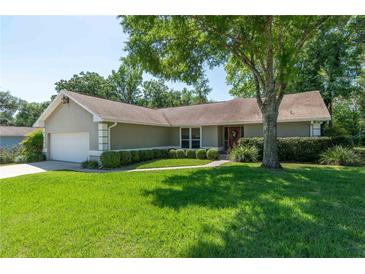 Charming single-story home with a well-manicured lawn, lush landscaping, and inviting red front door at 8120 Nw 48Th Ln, Ocala, FL 34482