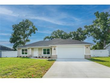 Charming single-story home with a well-manicured lawn, attached two-car garage, and a mix of stone and siding accents at 13588 Se 102Nd Ct, Belleview, FL 34420