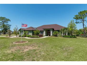 Sprawling single-story home featuring a manicured lawn, mature trees, and American flag at 6045 Ne 65Th St, Silver Springs, FL 34488