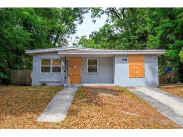 Exterior view of a single-story home with a gray exterior, boarded windows, and landscaping needs some attention at 1325 42Nd St, Orlando, FL 32839