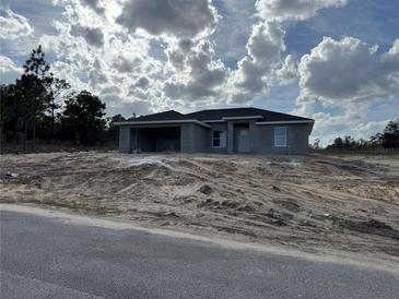 Unfinished single-story home with gray siding, a front yard covered with sand, and a cloudy sky at 4424 Sw Carnation Ct, Dunnellon, FL 34431