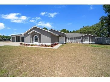 Charming gray home featuring a manicured lawn with fresh landscaping and a large garage at 9885 Se 144Th St, Summerfield, FL 34491