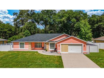 Charming coral home featuring a well-manicured lawn, attached garage, and stone accents at 1109 Ne 22Nd Ave, Ocala, FL 34470
