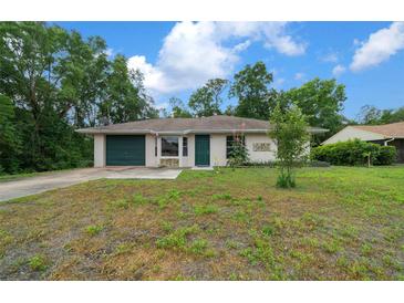 Charming single-story home featuring an attached garage, manicured lawn, and lush, mature trees at 21168 Sw Peach Blossom St, Dunnellon, FL 34431