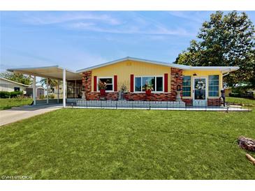 Charming yellow home features a well-manicured lawn and welcoming front porch, complemented by brick accents and a covered parking area at 9050 Sw 101St Ln, Ocala, FL 34481