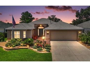 Charming single-story home with manicured lawn, landscaped flower beds, and inviting front porch, illuminated by beautiful twilight at 8545 Se 168Th Kittredge Loop, The Villages, FL 32162