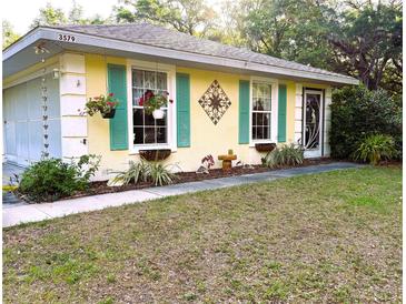 Charming exterior featuring a cheerful yellow facade, complemented by vibrant turquoise shutters and blossoming flower boxes at 3579 Sw Shorewood Dr, Dunnellon, FL 34431