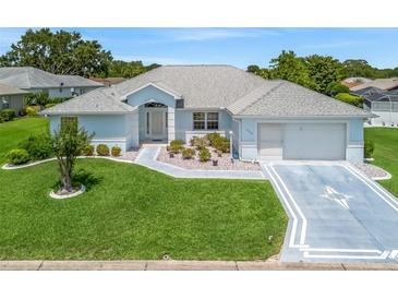 Charming single-story home with light blue exterior, well-manicured lawn and a two car garage on a sunny day at 17755 Se 117Th Cir, Summerfield, FL 34491