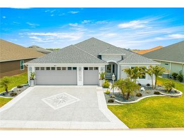 Charming single-story home featuring a well-manicured lawn, paver driveway, and a two-car garage under a bright blue sky at 907 Trifu Ter, The Villages, FL 32163