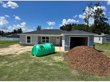 Single Gathering home showcasing its gray exterior, attached garage, green septic tank, and pile of mulch in yard at 1057 Nw 68Th Pl, Ocala, FL 34474