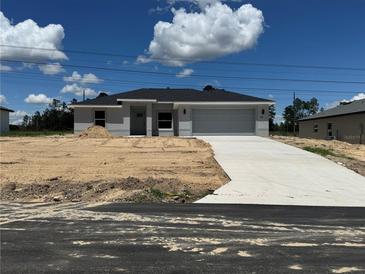 New construction home with a gray facade, a two-car garage, and a concrete driveway in a partially landscaped yard at 15419 Sw 65Th Terrace Rd, Ocala, FL 34473