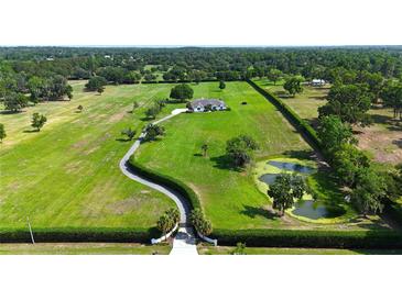 Expansive aerial view of estate home with a long driveway, lush green lawn, pond and mature trees at 601 Se 80Th St, Ocala, FL 34480