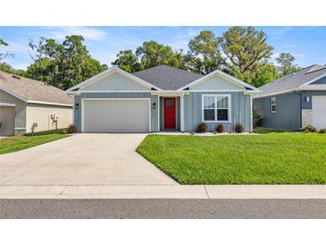 Charming single-story home with a well-manicured lawn, inviting red door, and attached garage at 6557 Se 4Th Ln, Ocala, FL 34472