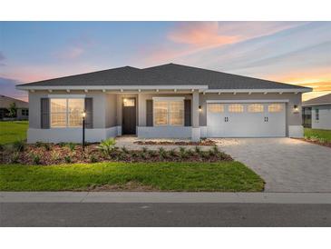 Charming single-story home featuring a well-manicured lawn and a two-car garage, illuminated by a picturesque sunset at 10977 Sw 101St Loop, Ocala, FL 34481