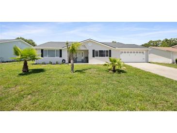 Charming home featuring a well-maintained lawn, an attached two-car garage, and beautiful landscaping with lovely palm trees at 8849 Sw 116Th Place Rd, Ocala, FL 34481