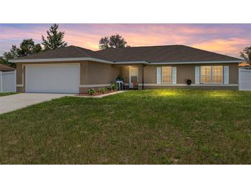 Charming single-story home with a well-manicured lawn and a two-car garage at sunset at 3887 Sw 156Th Pl, Ocala, FL 34473