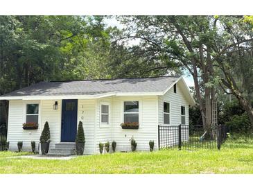 Charming white home with a dark blue front door, small front yard, black fence and mature trees at 1705 Nw 18Th Ave, Ocala, FL 34475