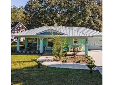 Charming teal home featuring a metal roof, inviting front porch, and well-maintained front lawn at 9330 Se 106Th Pl, Belleview, FL 34420