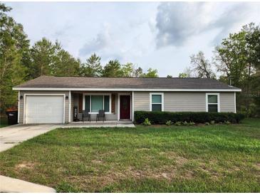 Charming single-story home with a well-manicured lawn, a red front door and an attached one car garage at 120 Fisher Ct, Ocklawaha, FL 32179