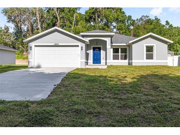 Charming home featuring a well-maintained lawn, a two-car garage, and an inviting bright blue front door at 12974 Se 42Nd Ct, Belleview, FL 34420