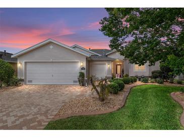 Charming single-story home featuring a manicured lawn, brick driveway, and well-maintained landscaping at dusk at 1748 Sw 157Th Place Rd, Ocala, FL 34473