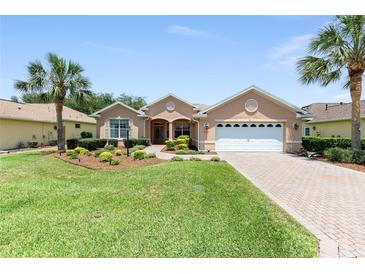 Charming single-story home featuring a well-manicured lawn, beautiful landscaping, and a brick-paved driveway at 8303 Sw 82Nd Cir, Ocala, FL 34481