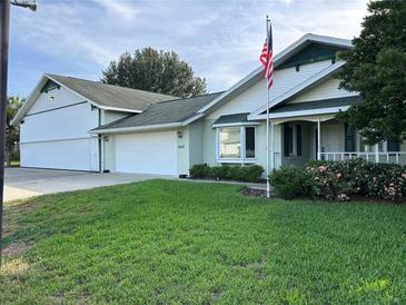 Charming single-story home with a lush green lawn and a three car garage with an American flag at 9622 Se 71St Ct, Ocala, FL 34472